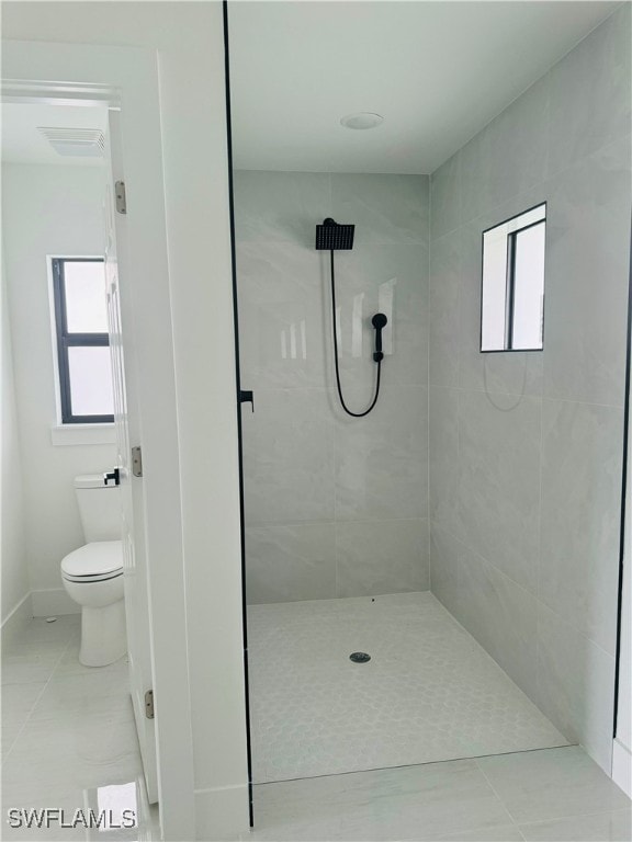 bathroom featuring tile patterned flooring, tiled shower, and toilet