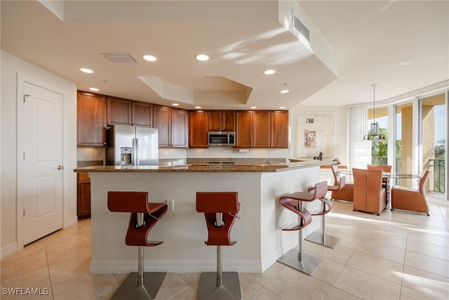 kitchen featuring stainless steel appliances, a kitchen breakfast bar, a center island with sink, decorative light fixtures, and light tile patterned floors