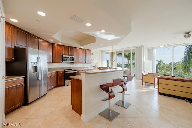 kitchen featuring light stone counters, appliances with stainless steel finishes, light tile patterned floors, and a breakfast bar