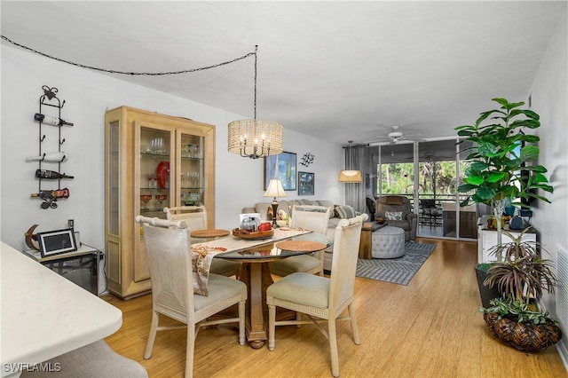 dining room with ceiling fan with notable chandelier and light wood-type flooring