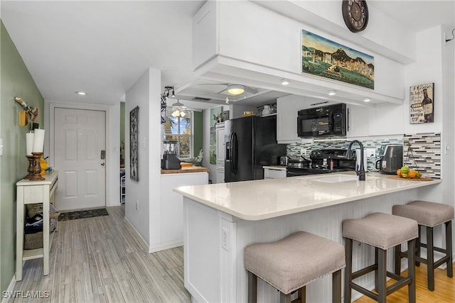 kitchen with kitchen peninsula, decorative backsplash, a breakfast bar, light wood-type flooring, and black appliances