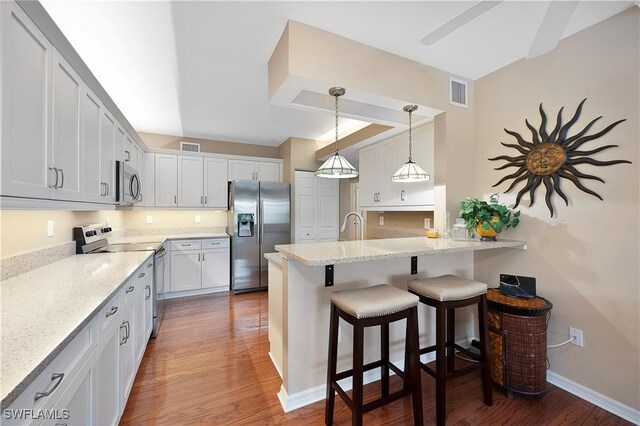 kitchen featuring light stone counters, appliances with stainless steel finishes, a breakfast bar area, white cabinets, and hardwood / wood-style flooring