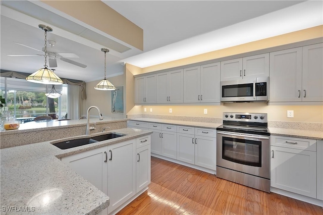 kitchen featuring sink, stainless steel appliances, light stone countertops, decorative light fixtures, and light wood-type flooring