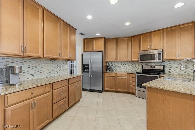 kitchen with sink, light tile patterned floors, appliances with stainless steel finishes, light stone counters, and decorative backsplash