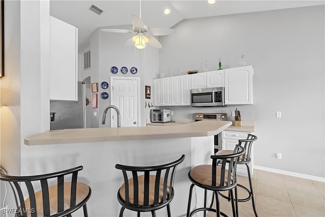 kitchen with white cabinets, light tile patterned flooring, kitchen peninsula, appliances with stainless steel finishes, and a kitchen bar