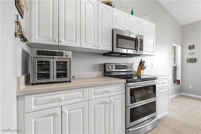 kitchen with light tile patterned flooring, vaulted ceiling, stainless steel appliances, and white cabinets