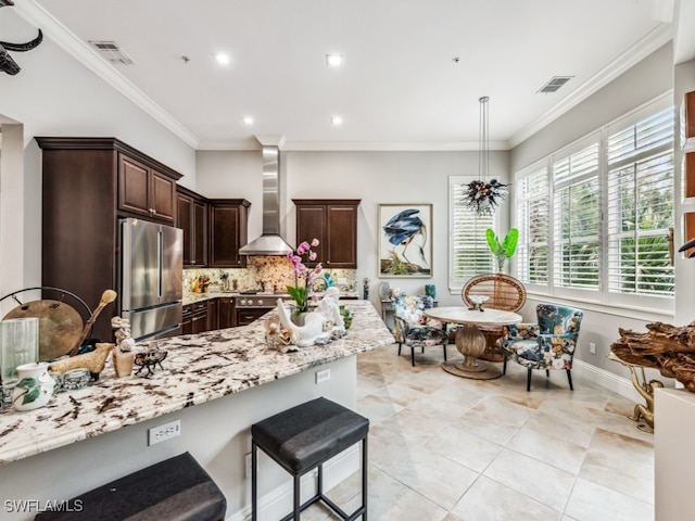 kitchen with wall chimney range hood, tasteful backsplash, crown molding, dark brown cabinetry, and stainless steel appliances