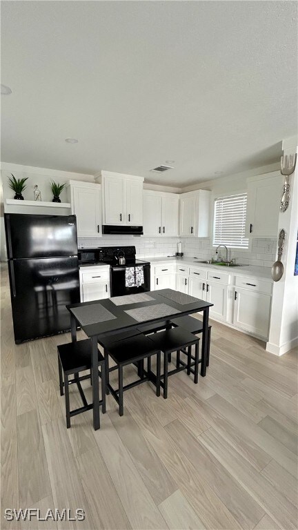 kitchen featuring tasteful backsplash, light hardwood / wood-style flooring, sink, black appliances, and white cabinetry