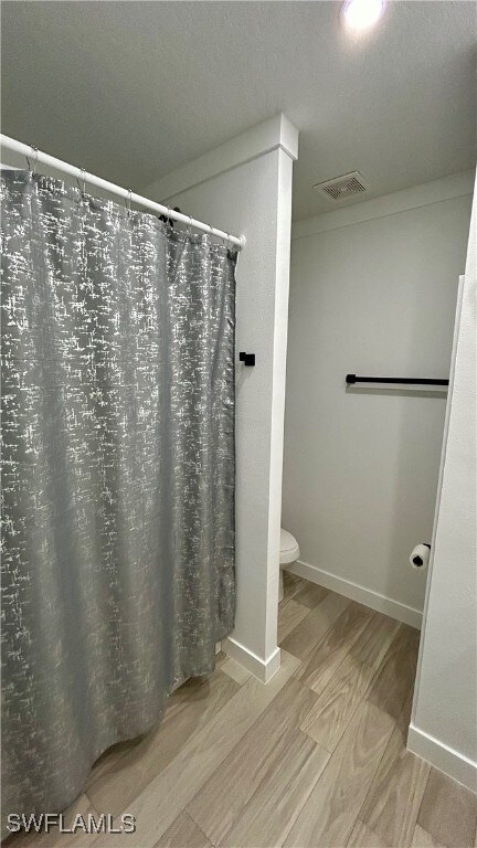 bathroom with toilet, hardwood / wood-style floors, and a shower with curtain