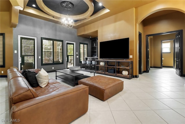 tiled living room featuring a high ceiling, a healthy amount of sunlight, a tray ceiling, and an inviting chandelier