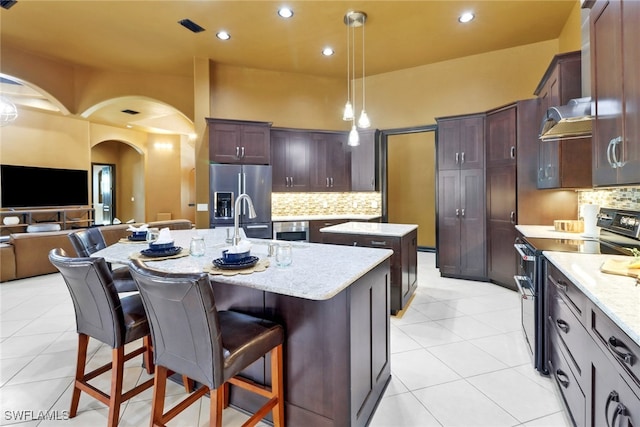 kitchen featuring light tile patterned floors, appliances with stainless steel finishes, decorative light fixtures, a breakfast bar, and a center island with sink