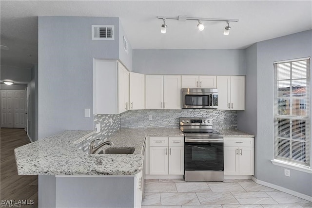 kitchen with sink, light stone countertops, stainless steel appliances, kitchen peninsula, and white cabinets