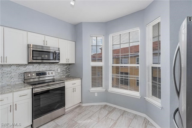 kitchen featuring light stone countertops, decorative backsplash, stainless steel appliances, and white cabinets