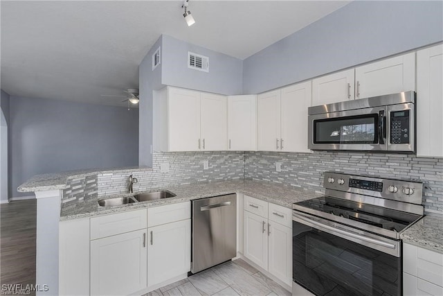 kitchen featuring white cabinets, sink, kitchen peninsula, appliances with stainless steel finishes, and light stone countertops