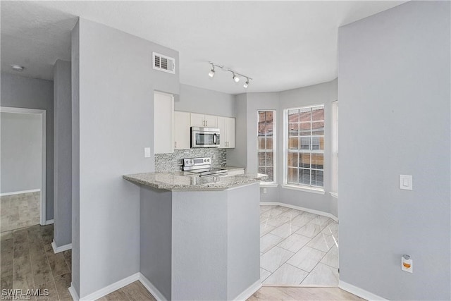 kitchen with kitchen peninsula, white cabinetry, appliances with stainless steel finishes, light stone countertops, and decorative backsplash