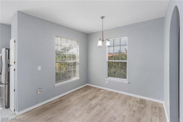 unfurnished dining area featuring a notable chandelier, light wood-type flooring, and a healthy amount of sunlight