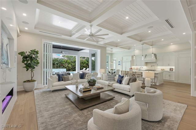 living room with crown molding, light hardwood / wood-style floors, coffered ceiling, ceiling fan, and beam ceiling