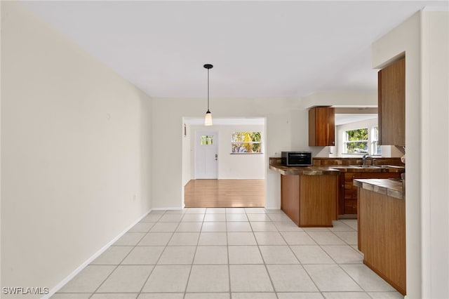 kitchen with kitchen peninsula, hanging light fixtures, sink, and light tile patterned floors