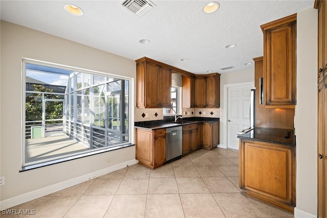 kitchen featuring dishwasher, sink, tasteful backsplash, dark stone counters, and light tile patterned floors