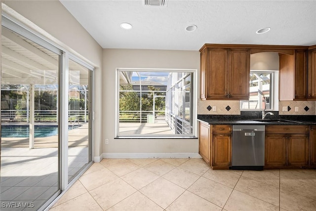 kitchen featuring sink, stainless steel dishwasher, backsplash, dark stone counters, and light tile patterned flooring