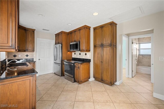 kitchen featuring sink, decorative backsplash, dark stone countertops, light tile patterned floors, and stainless steel appliances