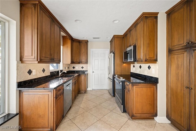 kitchen with sink, stainless steel appliances, dark stone countertops, decorative backsplash, and light tile patterned flooring