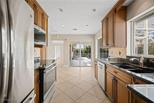 kitchen featuring sink, dark stone countertops, light tile patterned floors, appliances with stainless steel finishes, and tasteful backsplash