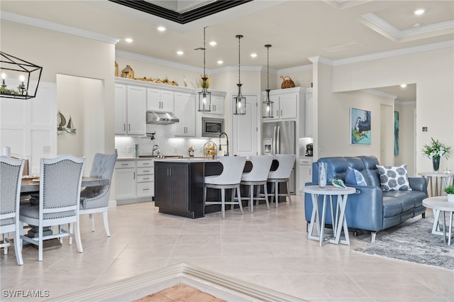 kitchen with decorative backsplash, appliances with stainless steel finishes, a kitchen island with sink, decorative light fixtures, and white cabinets