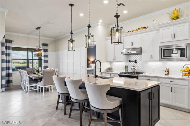 kitchen featuring a center island with sink, white cabinets, stainless steel appliances, and decorative light fixtures