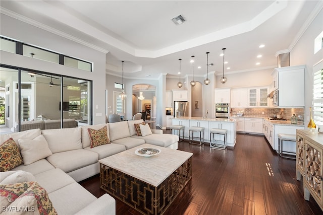 living room featuring dark wood-type flooring, ornamental molding, a tray ceiling, and an inviting chandelier