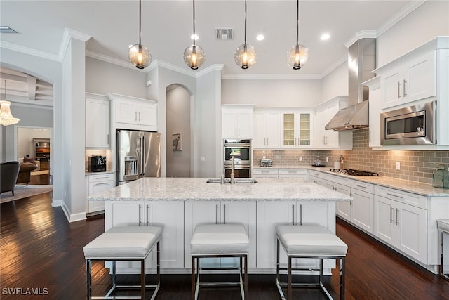 kitchen with an island with sink, stainless steel appliances, wall chimney exhaust hood, white cabinets, and dark hardwood / wood-style floors