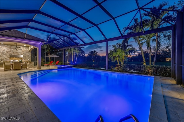 pool at dusk featuring exterior kitchen, a patio, and a lanai