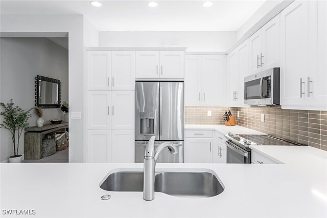 kitchen with appliances with stainless steel finishes, tasteful backsplash, sink, and white cabinets