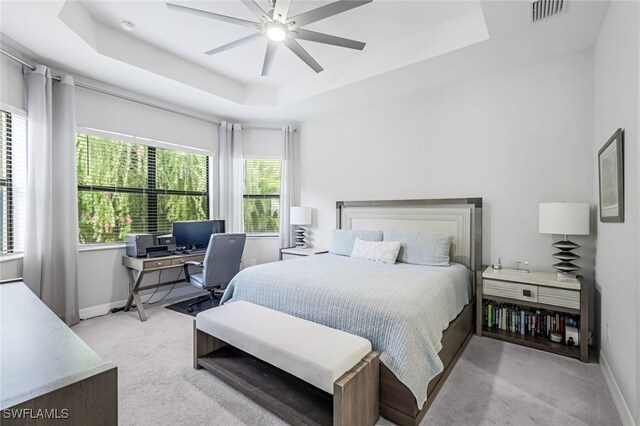 bedroom with ceiling fan, a tray ceiling, and light colored carpet