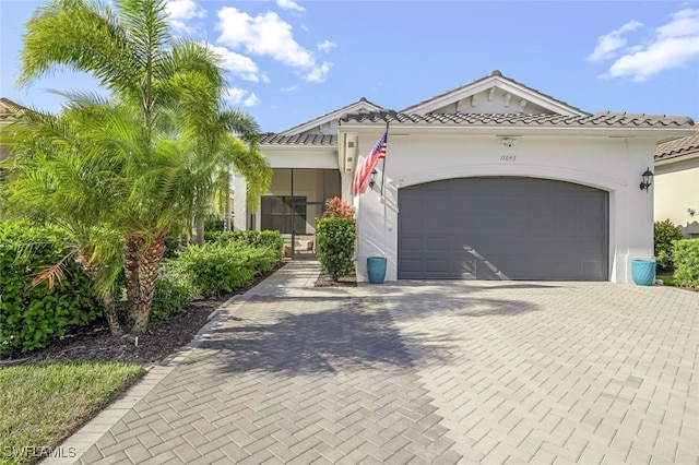 view of front facade featuring a garage, decorative driveway, a tile roof, and stucco siding