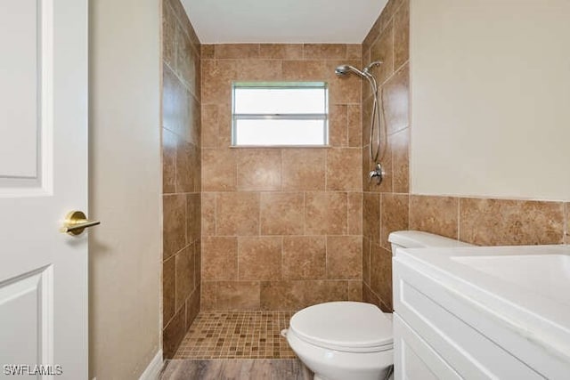 bathroom featuring vanity, hardwood / wood-style floors, toilet, and tiled shower