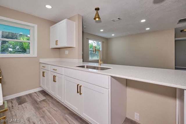 kitchen with light wood-type flooring, sink, kitchen peninsula, white cabinetry, and decorative light fixtures