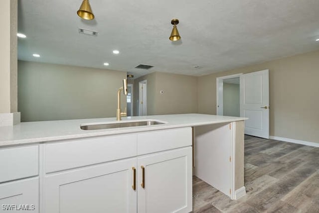 kitchen with light hardwood / wood-style flooring, white cabinets, decorative light fixtures, and sink