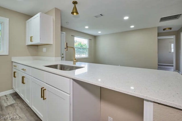 kitchen with light hardwood / wood-style floors, light stone countertops, sink, and white cabinets