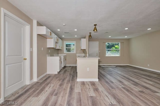 kitchen with light wood-type flooring, sink, a kitchen island, and white cabinets