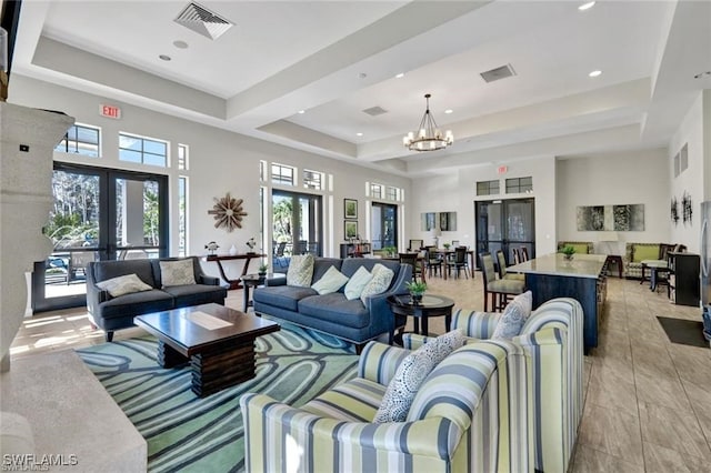 living area featuring french doors, a tray ceiling, visible vents, and a notable chandelier