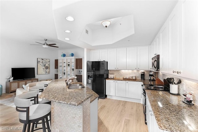 kitchen featuring a raised ceiling, stainless steel range with electric stovetop, black fridge with ice dispenser, and white cabinetry