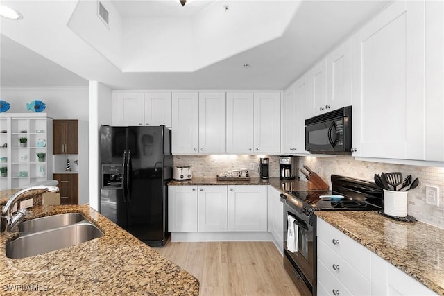 kitchen featuring light stone counters, sink, white cabinets, and black appliances