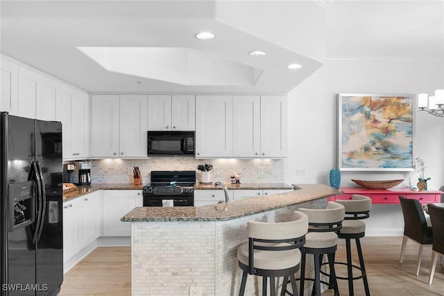 kitchen with black appliances, decorative backsplash, white cabinets, and stone counters