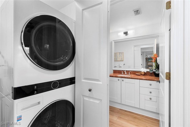 clothes washing area with sink, stacked washer and dryer, and light wood-type flooring