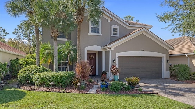 view of front facade featuring a front yard, an attached garage, stucco siding, a tiled roof, and decorative driveway