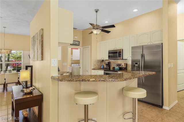 kitchen with kitchen peninsula, washer / clothes dryer, stainless steel appliances, dark stone countertops, and a kitchen bar