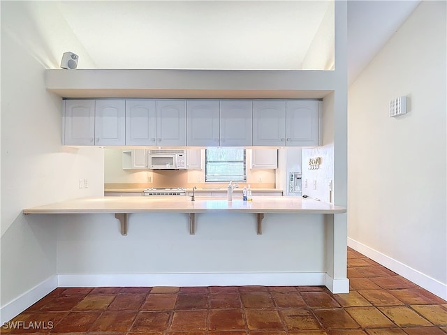 kitchen featuring kitchen peninsula, vaulted ceiling, a kitchen bar, and white cabinetry