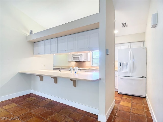 kitchen with a breakfast bar area, kitchen peninsula, white appliances, and white cabinetry