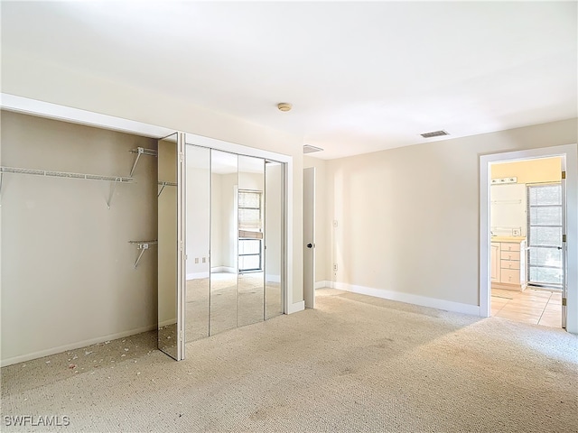 unfurnished bedroom with light colored carpet, ensuite bath, multiple windows, and two closets